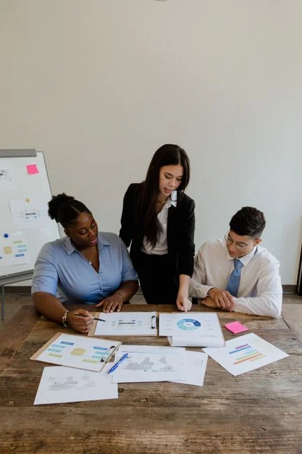 Three businesswomen collaborate with graphs and a laptop in a modern office setting.